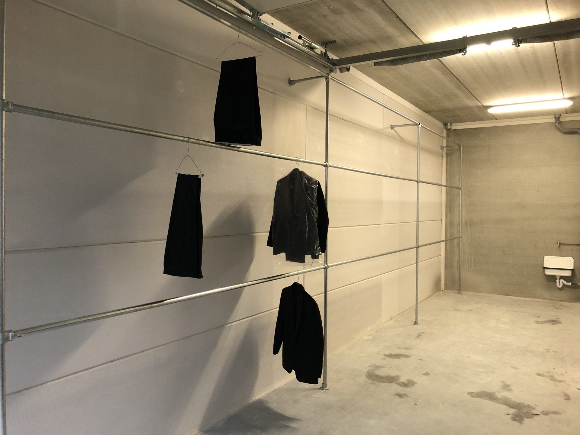 Kleding hangt aan een metalen rek in een kamer met witte muren.