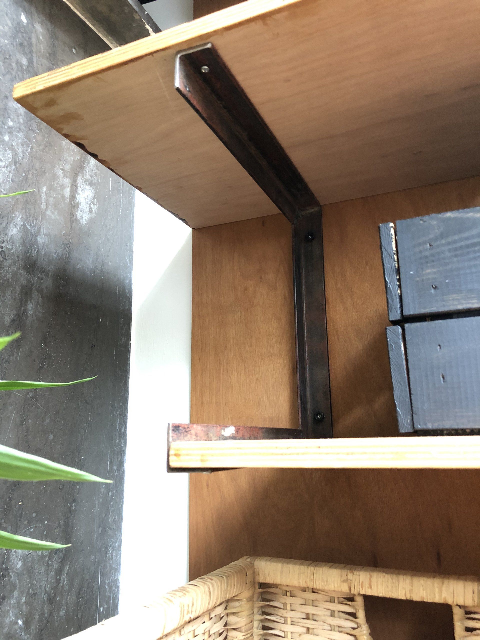 Houten planken met metalen beugels, waarbij een plank wordt ondersteund door een verticaal stuk.