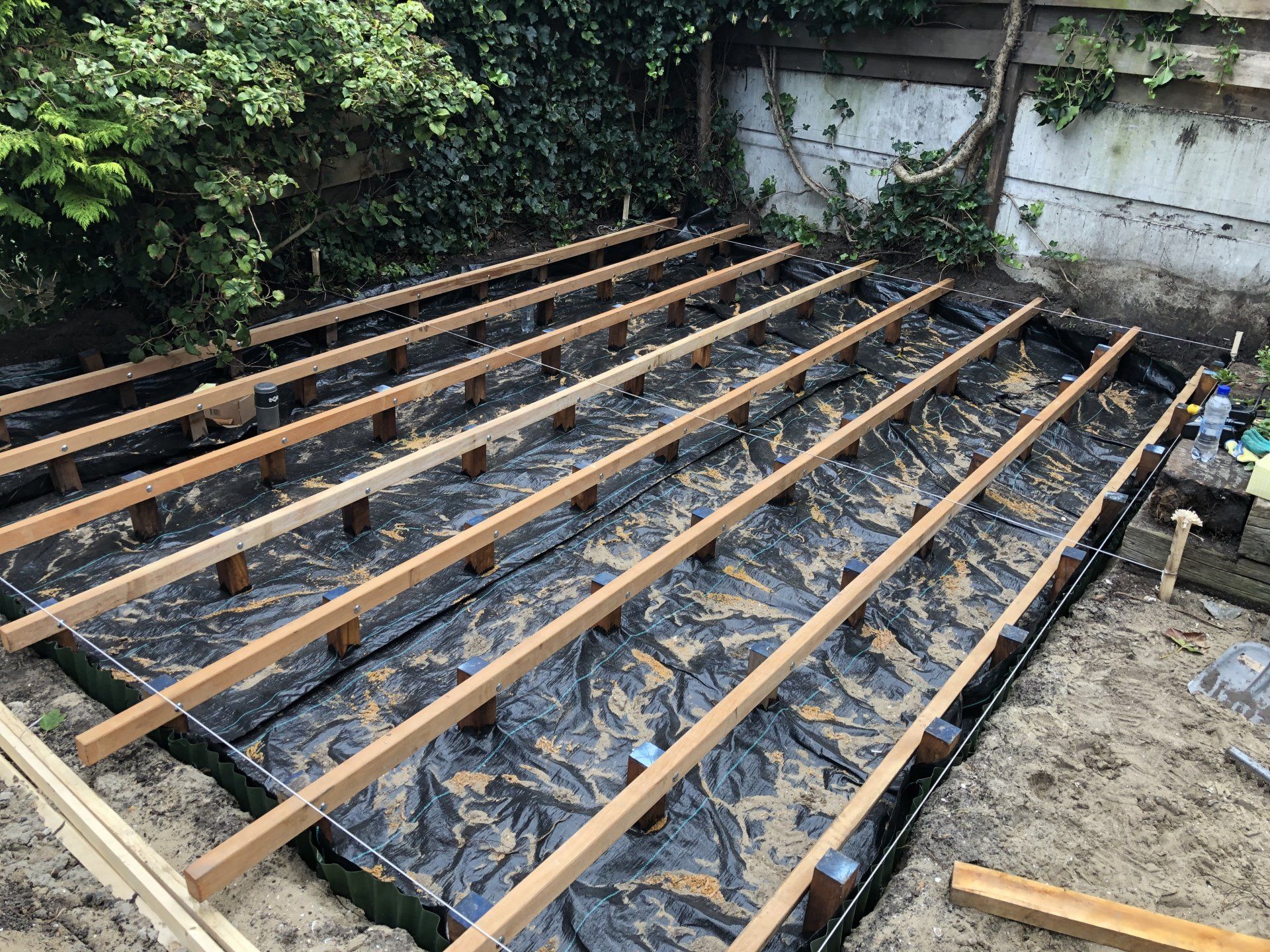 Houten terrasconstructie in aanbouw in een tuin, rustend op zwart doek.