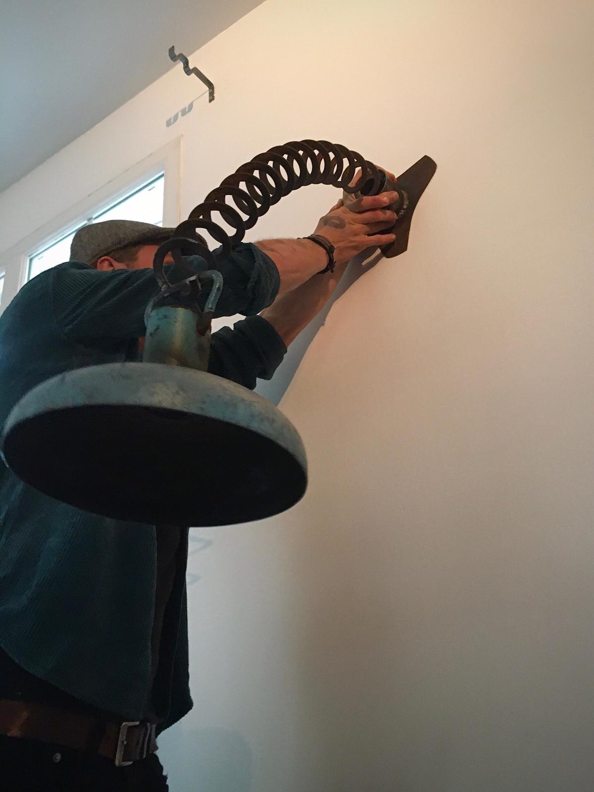 Iemand installeert een lamp met flexibele arm aan een witte muur.