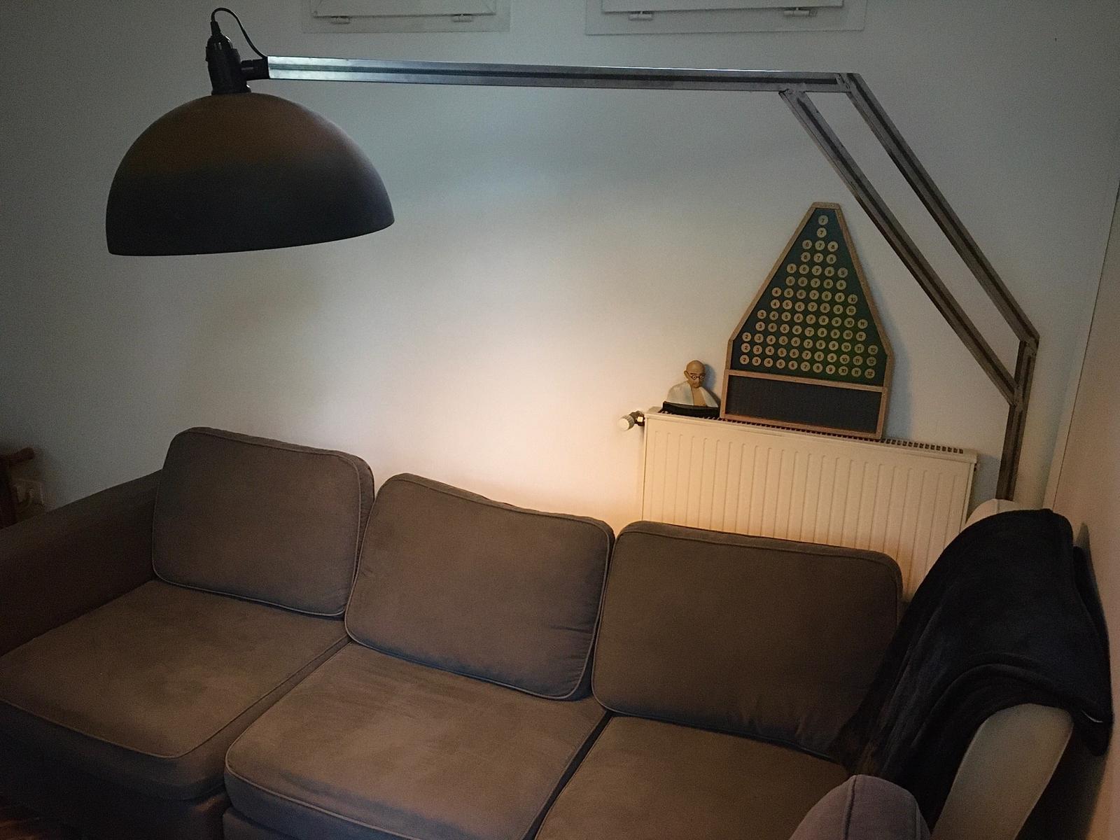Grijze bank onder een gebogen metalen vloerlamp met een zwarte lampenkap. De setting is binnenshuis.