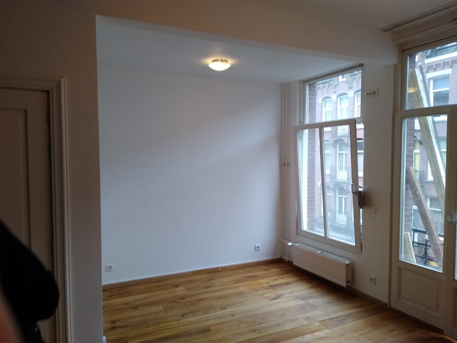 Lege kamer met houten vloer, witte muren en een groot raam.