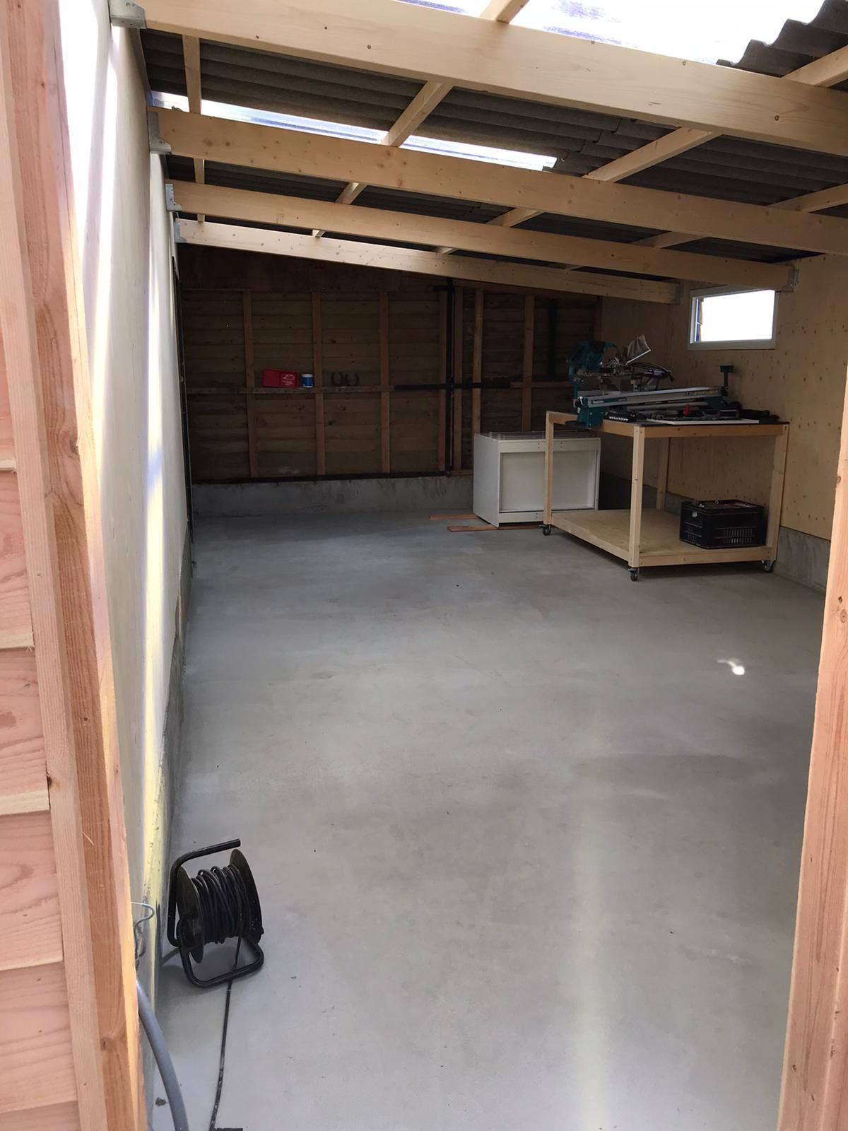 Garage-interieur, betonnen vloer, houten frame, gereedschap op een tafel en een stroomkabel op de vloer.