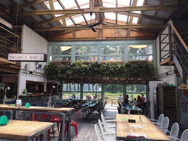Binnenrestaurant met tafels en stoelen, grote ramen en dakramen, vol met gasten.