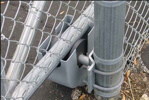 Chain-link fence post with gray metal bracket and plastic housing at the base