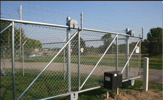 Chain-link fence gate at a sports field, with diagonal braces and a black control box.