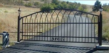 Black wrought-iron gate with arched top blocking a road in a rural area