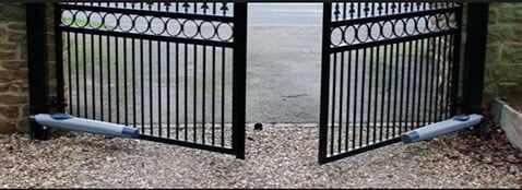 Black iron gate opened to a lakeside walkway with gravel ground and water beyond.