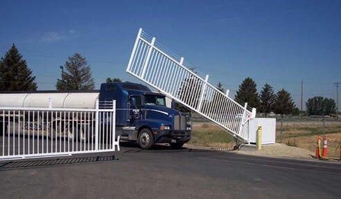 Blue truck pushing open a white gate at a roadside entrance under a clear sky