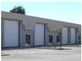 Garage Door Installation Service — Guaranteed Door Service, Inc. Gray industrial warehouse with roll-up doors and a few small windows in a parking lot