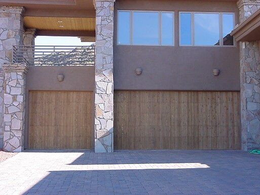 Modern house exterior with two wooden garage doors and stone columns in bright sunlight