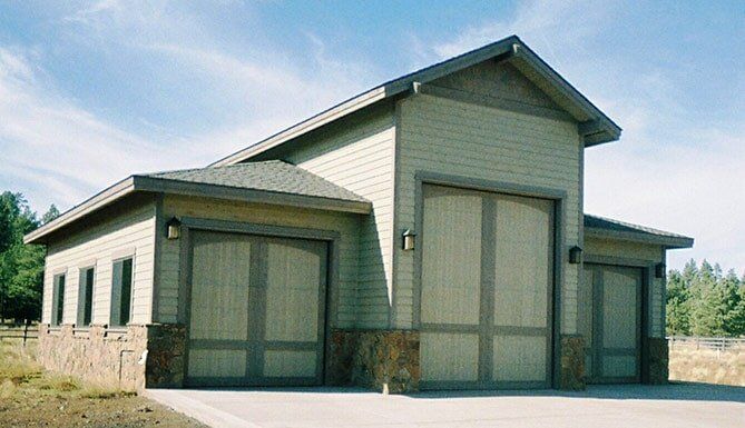Small green utility building with tan trim and large double doors on a sunny day