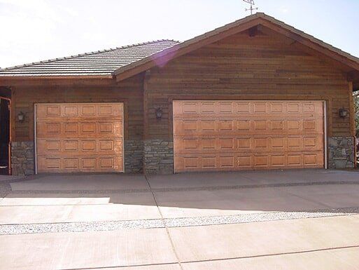 Two-car wooden garage with brown doors and brick accents under a gabled roof