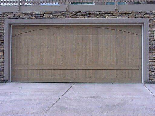 Closed beige garage door on a concrete driveway under a stone wall.