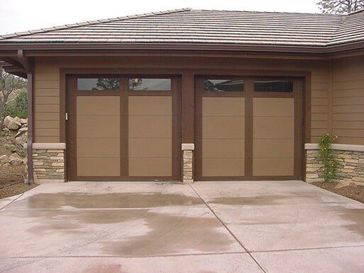 Two brown garage doors on a tan house with a concrete driveway in front.