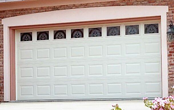 White double garage door with small arched windows on a brick house exterior