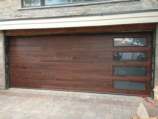 Dark wood garage door with small windows, set in a stone-and-brick exterior.