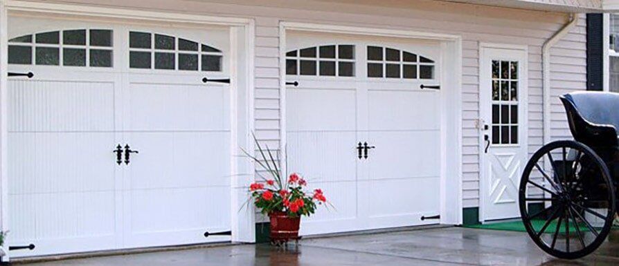 White double garage doors with a flower pot and a decorative wagon wheel by the entrance