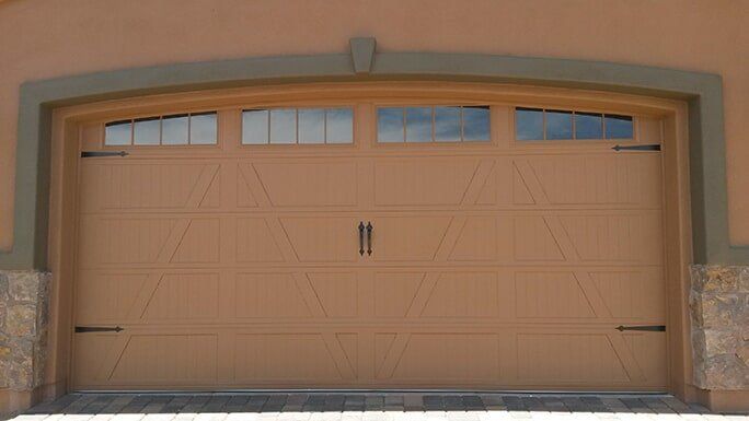 Tan double garage door with small windows on a stucco house exterior