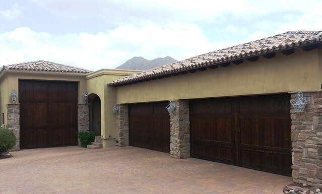 Adobe-style house with stone pillars, brown garage doors, and tiled roofs in a desert setting