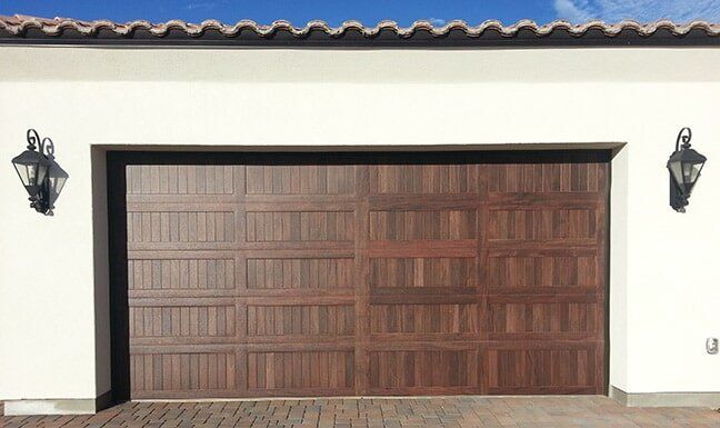 Wooden double garage door in a white stucco wall with black lanterns on either side.