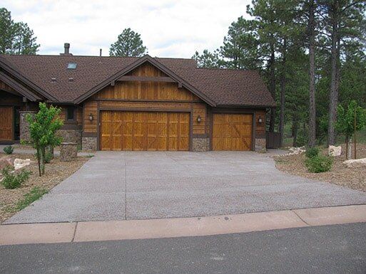 Suburban house with a large wooden garage and concrete driveway surrounded by trees and desert landscaping
