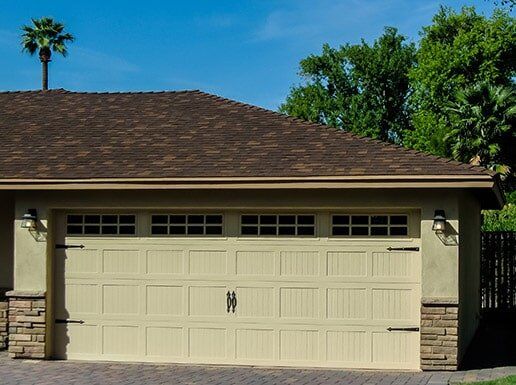 Single-story house with a beige garage door, brown roof, and palm tree in front