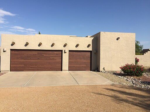 Modern beige house with two brown garage doors, desert landscaping, and a clear blue sky