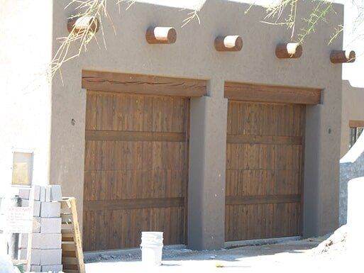 Two large wooden doors on a beige stucco building with small wall lights above them.