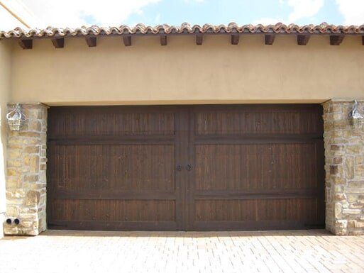 Closed dark brown wooden double garage door set in a stucco wall with stone sides and a tiled roof overhang