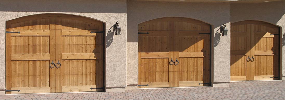 Three wooden garage doors under a stucco archway in sunlight