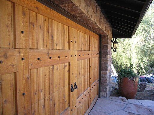 Wooden barn-style garage doors with black handles under a sloped roof, beside a clay pot outdoors