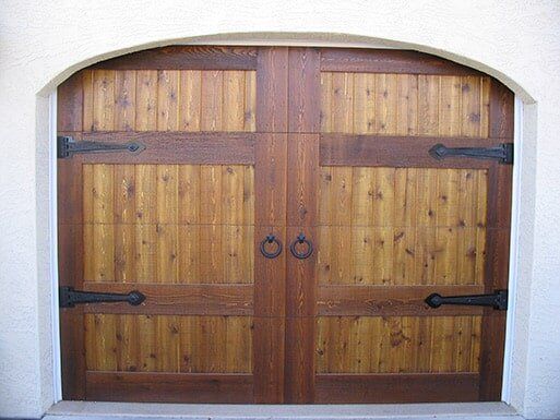 Wooden double garage doors with black hinges set in a white stucco archway