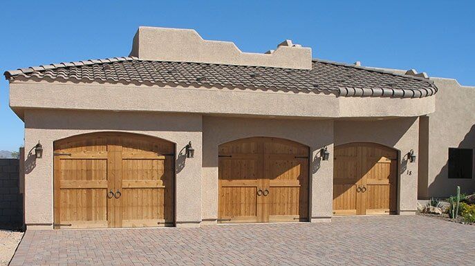 Three-car beige stucco garage with wooden doors and tiled roof in a sunny driveway