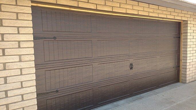 Brown garage door set in a tan brick wall, viewed from the sidewalk.