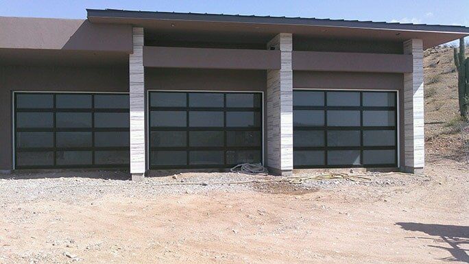 Modern building facade with three dark garage doors and a gravel foreground