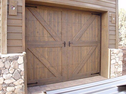 Closed wooden garage door with diagonal bracing, framed by stone and wood siding.