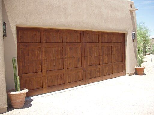 Large wooden garage door on a stucco house with potted plants beside it