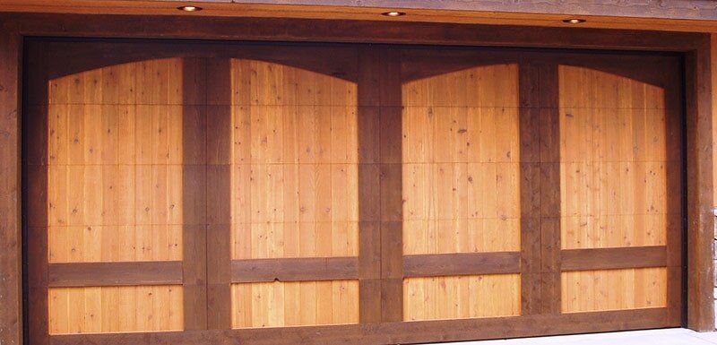 Wooden arched garage door with four window panels, lit by sunlight