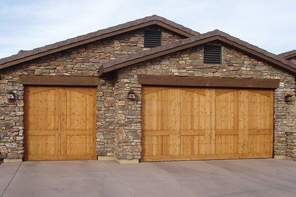 Stone house with two wooden garage doors and a paved driveway