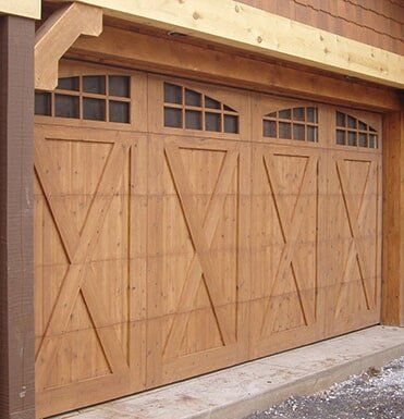 Wooden garage door with diagonal X-bracing and small arched windows under a stucco overhang