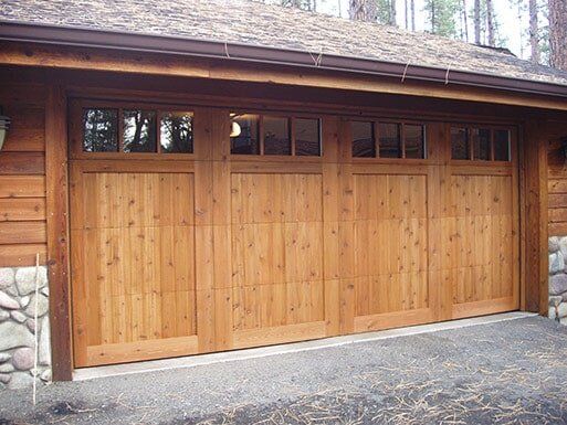 Wooden garage door with small windows, set in a stone-and-wood exterior beside a paved driveway.