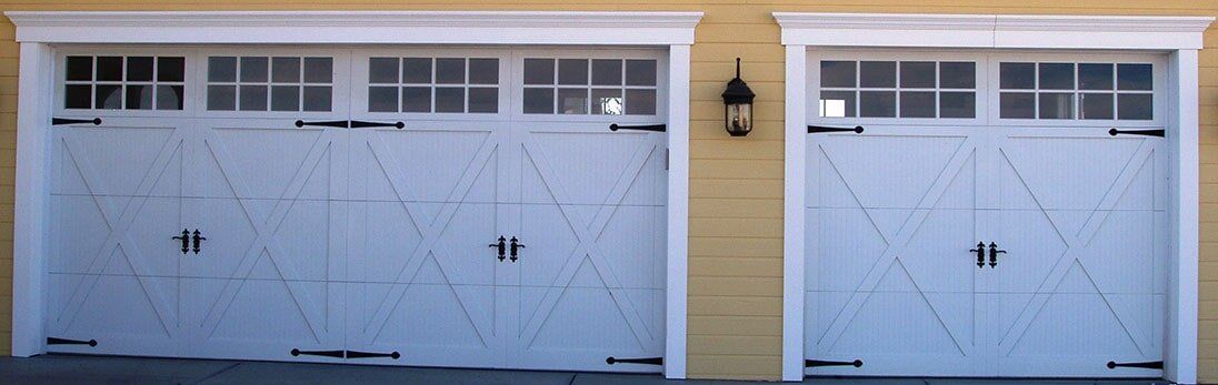 Two light blue garage doors with white windows on a yellow house exterior