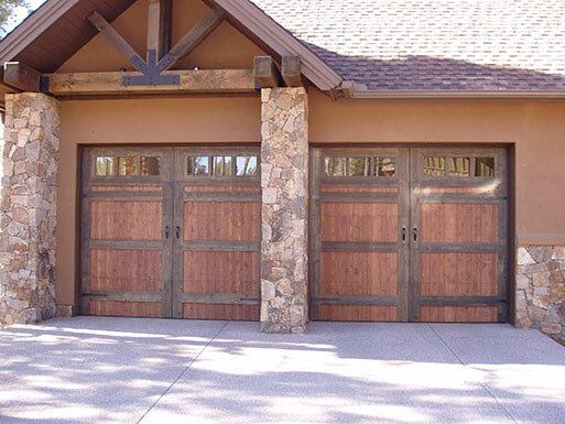 Two wooden garage doors framed by stone columns on a tan house exterior