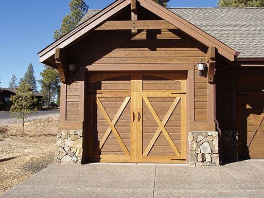 Wooden double garage doors on a rustic cabin with stone pillars and a concrete driveway
