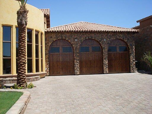 Sunlit stucco house with three wooden garage doors and a palm tree by the driveway