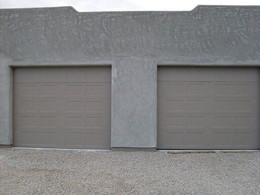 Two closed gray garage doors on a concrete building facade