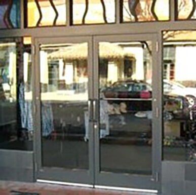 Glass storefront entrance with double doors and reflections of parked cars outside