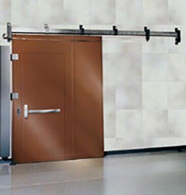Brown door in a tiled room with a black sliding rail across the top and a silver handle