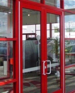 Red glass entry doors with silver handles and a view into a store interior